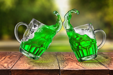 Image showing Splashes of fresh green beer in two jumping glasses.