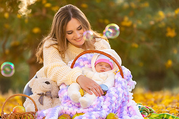 Image showing Mom happily looks at the two-month-old baby sleeping in a basket, flying soap bubbles