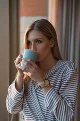 Image showing young woman enjoying evening coffee by the window