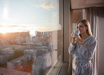 Image showing young woman enjoying evening coffee by the window