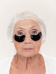 Image showing Senior woman at studio isolated on white wall looking at camera and making masks under eyes