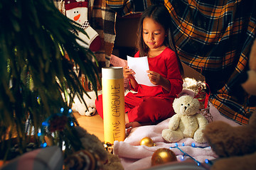 Image showing Merry Christmas and Happy Holidays. Cute little child girl writes the letter to Santa Claus near Christmas tree