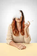 Image showing Tranquil woman sitting and smoking resting at the table. Cloud of smoke covering her face. Copy space