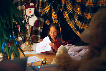 Image showing Merry Christmas and Happy Holidays. Cute little child girl writes the letter to Santa Claus near Christmas tree