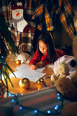 Image showing Merry Christmas and Happy Holidays. Cute little child girl writes the letter to Santa Claus near Christmas tree