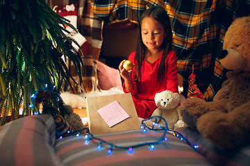 Image showing Merry Christmas and Happy Holidays. Cute little child girl writes the letter to Santa Claus near Christmas tree