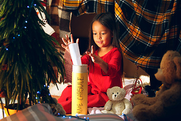 Image showing Merry Christmas and Happy Holidays. Cute little child girl writes the letter to Santa Claus near Christmas tree