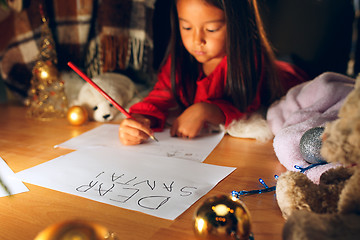 Image showing Merry Christmas and Happy Holidays. Cute little child girl writes the letter to Santa Claus near Christmas tree