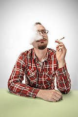 Image showing Handsome hipster man smoking cigarette at home. Man looking upwards and enjoying spending free time.