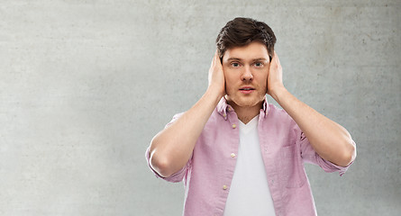 Image showing man closing ears by hands over gray concrete wall