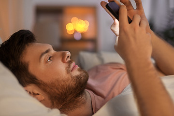 Image showing young man with smartphone in bed at night