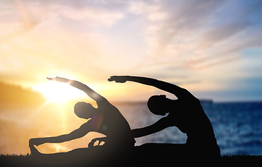 Image showing couple doing yoga over sunset sea background