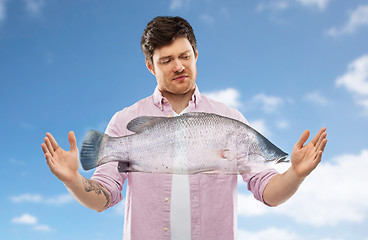 Image showing displeased young man showing size of fish over sky