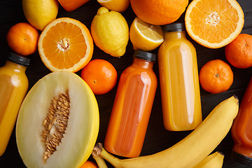 Image showing Mix of orange and yellow colored fruits and juices on black wood