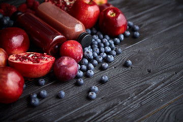 Image showing Various fresh red, purple black fruits. Mix of fruits and bottled juices on black