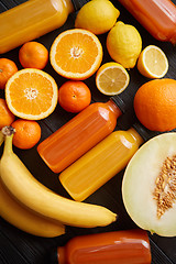 Image showing Mix of orange and yellow colored fruits and juices on black wood