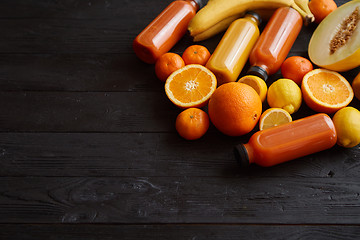 Image showing Yellow and orange fruits and botteled juices placed on black woo