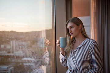 Image showing young woman enjoying evening coffee by the window