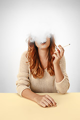 Image showing Tranquil woman sitting and smoking resting at the table. Cloud of smoke covering her face. Copy space