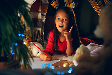 Image showing Merry Christmas and Happy Holidays. Cute little child girl writes the letter to Santa Claus near Christmas tree