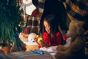 Image showing christmas, holidays and childhood concept - happy girl in red clothes decorating natural fir tree