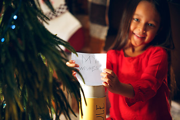 Image showing Merry Christmas and Happy Holidays. Cute little child girl writes the letter to Santa Claus near Christmas tree