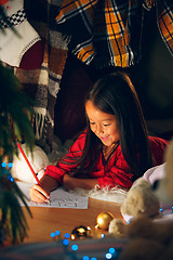 Image showing Merry Christmas and Happy Holidays. Cute little child girl writes the letter to Santa Claus near Christmas tree