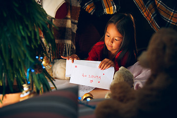 Image showing Merry Christmas and Happy Holidays. Cute little child girl writes the letter to Santa Claus near Christmas tree