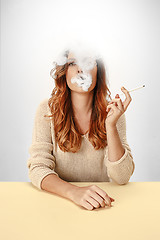 Image showing Tranquil woman sitting and smoking resting at the table. Cloud of smoke covering her face. Copy space