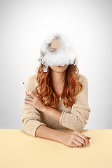 Image showing Tranquil woman sitting and smoking resting at the table. Cloud of smoke covering her face. Copy space