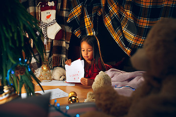 Image showing Merry Christmas and Happy Holidays. Cute little child girl writes the letter to Santa Claus near Christmas tree