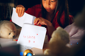 Image showing Merry Christmas and Happy Holidays. Cute little child girl writes the letter to Santa Claus near Christmas tree