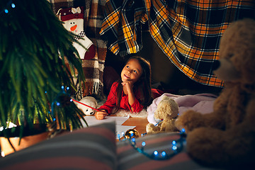 Image showing Merry Christmas and Happy Holidays. Cute little child girl writes the letter to Santa Claus near Christmas tree