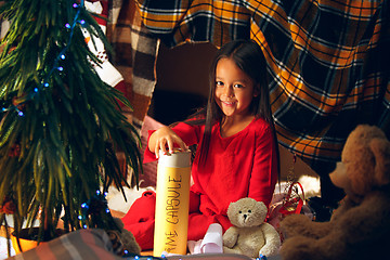 Image showing Merry Christmas and Happy Holidays. Cute little child girl writes the letter to Santa Claus near Christmas tree