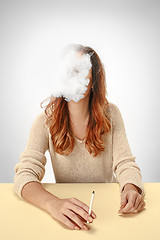 Image showing Tranquil woman sitting and smoking resting at the table. Cloud of smoke covering her face. Copy space