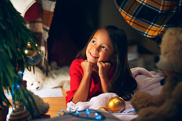 Image showing christmas, holidays and childhood concept - happy girl in red clothes decorating natural fir tree