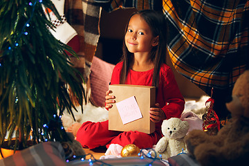 Image showing Merry Christmas and Happy Holidays. Cute little child girl writes the letter to Santa Claus near Christmas tree