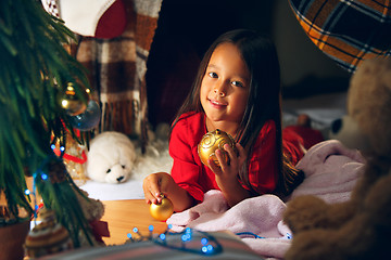 Image showing christmas, holidays and childhood concept - happy girl in red clothes decorating natural fir tree