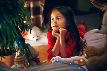 Image showing christmas, holidays and childhood concept - happy girl in red clothes decorating natural fir tree