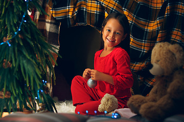 Image showing christmas, holidays and childhood concept - happy girl in red clothes decorating natural fir tree