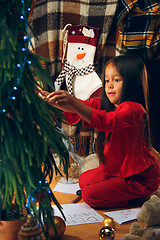 Image showing christmas, holidays and childhood concept - happy girl in red clothes decorating natural fir tree