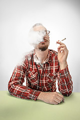 Image showing Handsome hipster man smoking cigarette at home. Man looking upwards and enjoying spending free time.