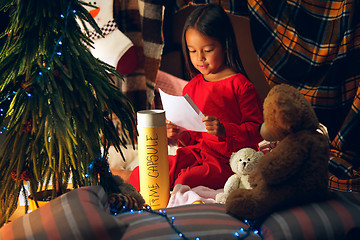 Image showing Merry Christmas and Happy Holidays. Cute little child girl writes the letter to Santa Claus near Christmas tree