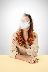 Image showing Tranquil woman sitting and smoking resting at the table. Cloud of smoke covering her face. Copy space