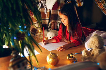 Image showing Merry Christmas and Happy Holidays. Cute little child girl writes the letter to Santa Claus near Christmas tree