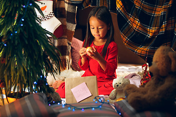 Image showing Merry Christmas and Happy Holidays. Cute little child girl writes the letter to Santa Claus near Christmas tree