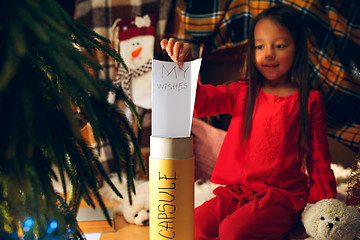 Image showing Merry Christmas and Happy Holidays. Cute little child girl writes the letter to Santa Claus near Christmas tree