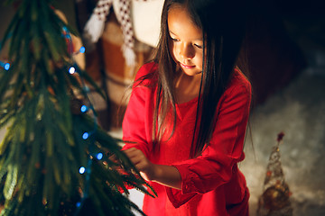 Image showing christmas, holidays and childhood concept - happy girl in red clothes decorating natural fir tree