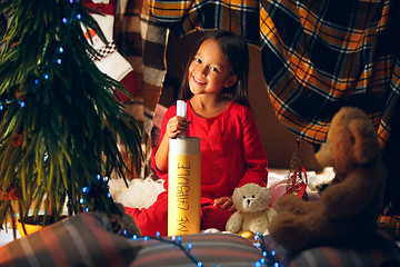 Image showing Merry Christmas and Happy Holidays. Cute little child girl writes the letter to Santa Claus near Christmas tree