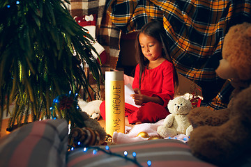 Image showing Merry Christmas and Happy Holidays. Cute little child girl writes the letter to Santa Claus near Christmas tree